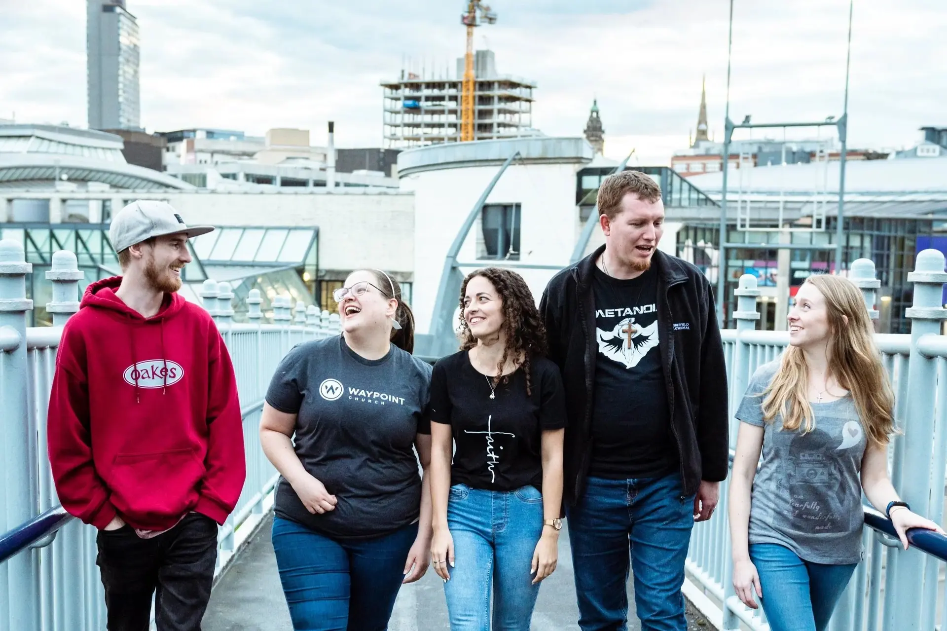 A group of friends walking and talking together on a bridge overlooking the Sheffield skyline
